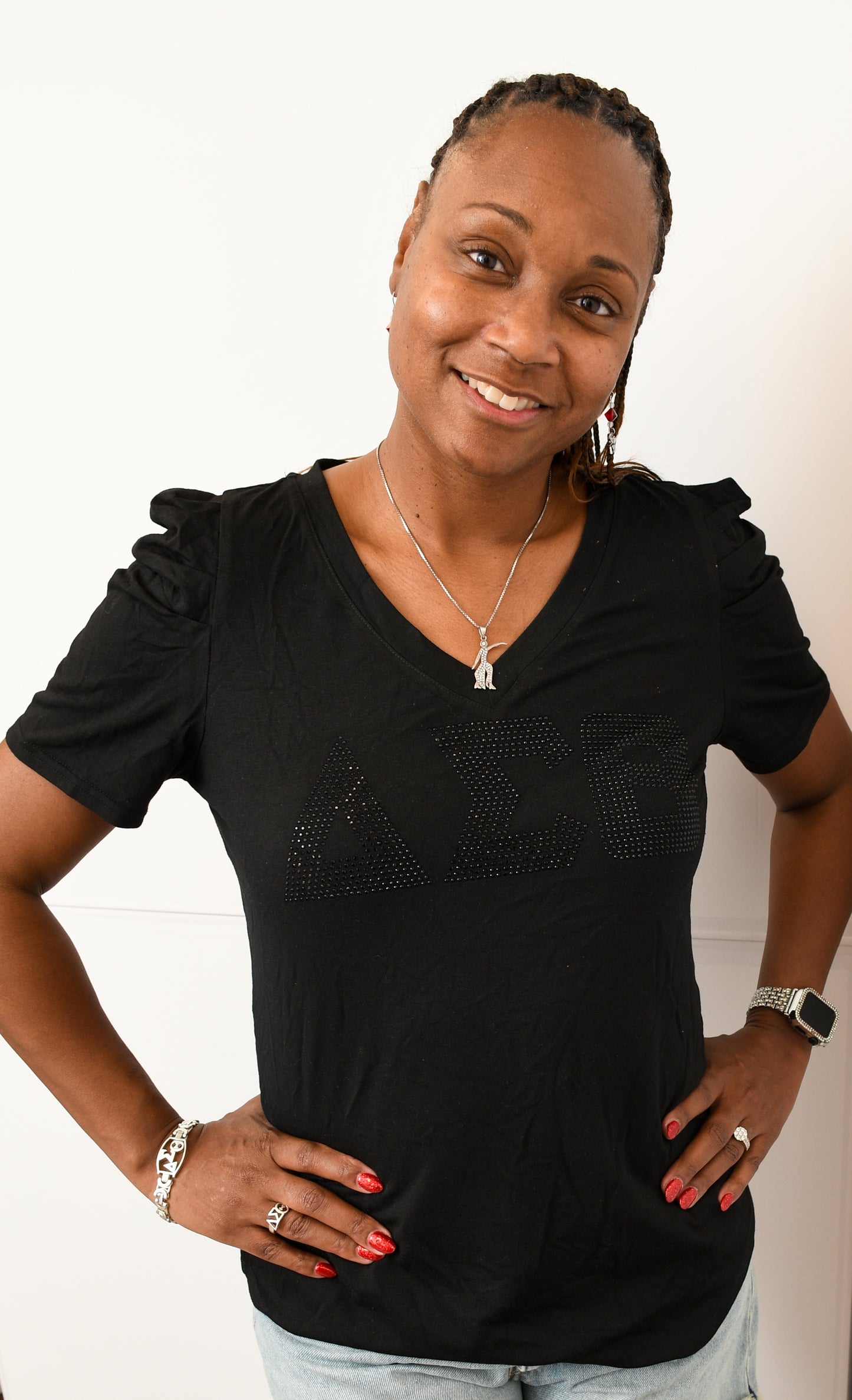 Woman wearing a ruffled sleeved black top with DST symbols in black rhinestones with her back up against a white background