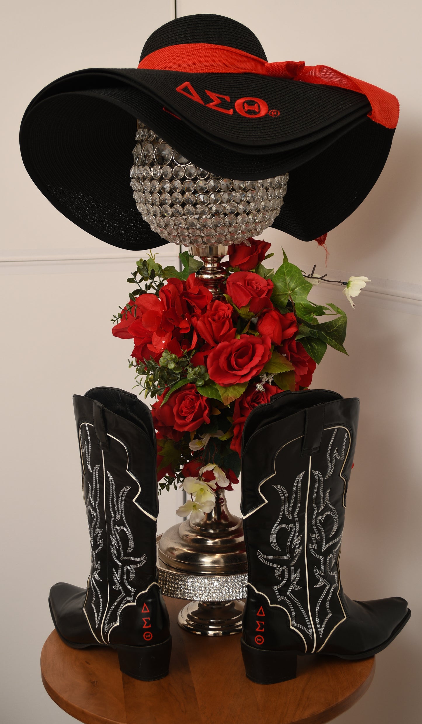 Decorative display with black hat, cowboy boots, and bouquet of red flowers on a white background