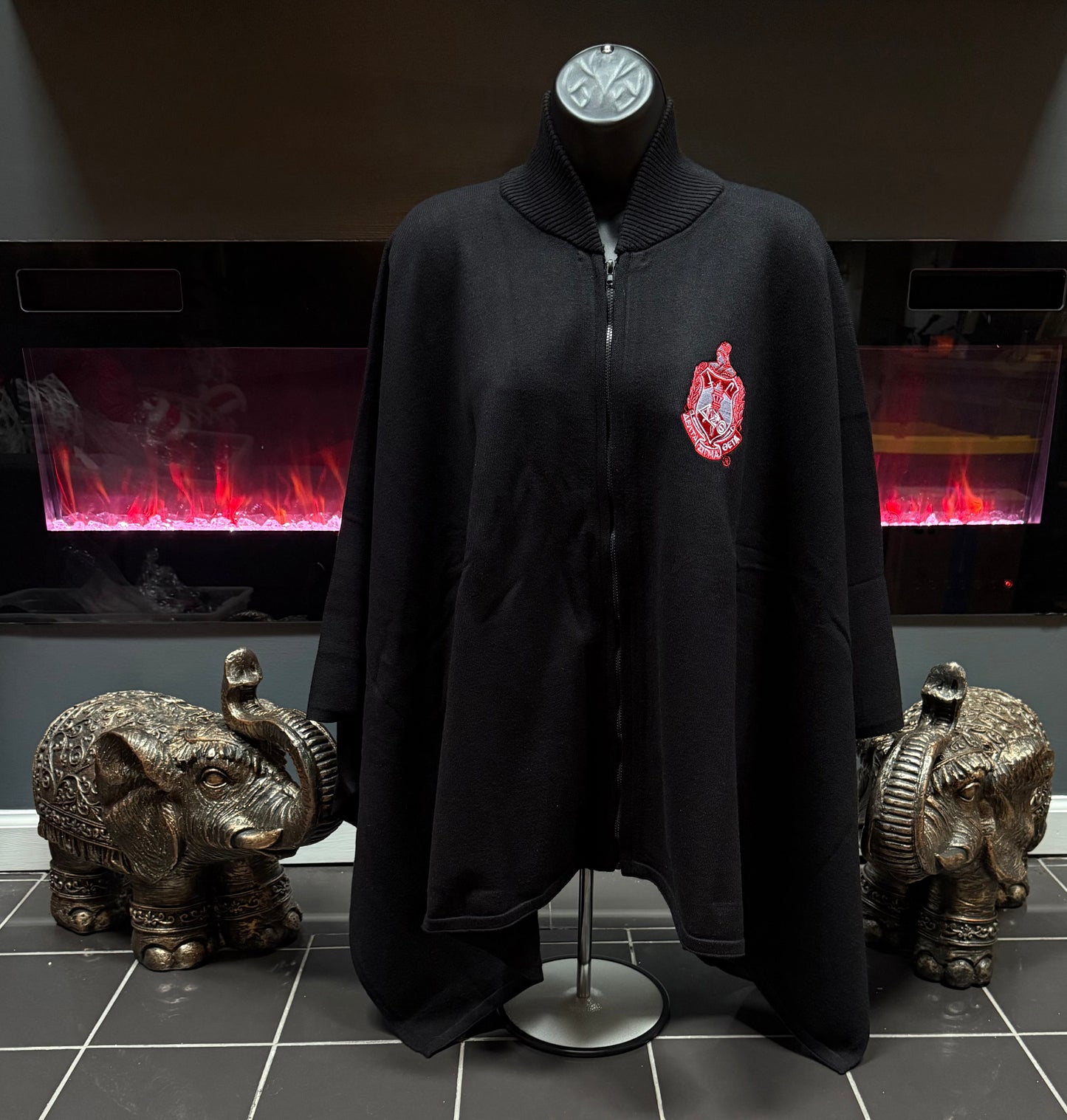 A black zip-front cape with a ribbed mock neck and a DST embroidered sorority shield on the left chest.